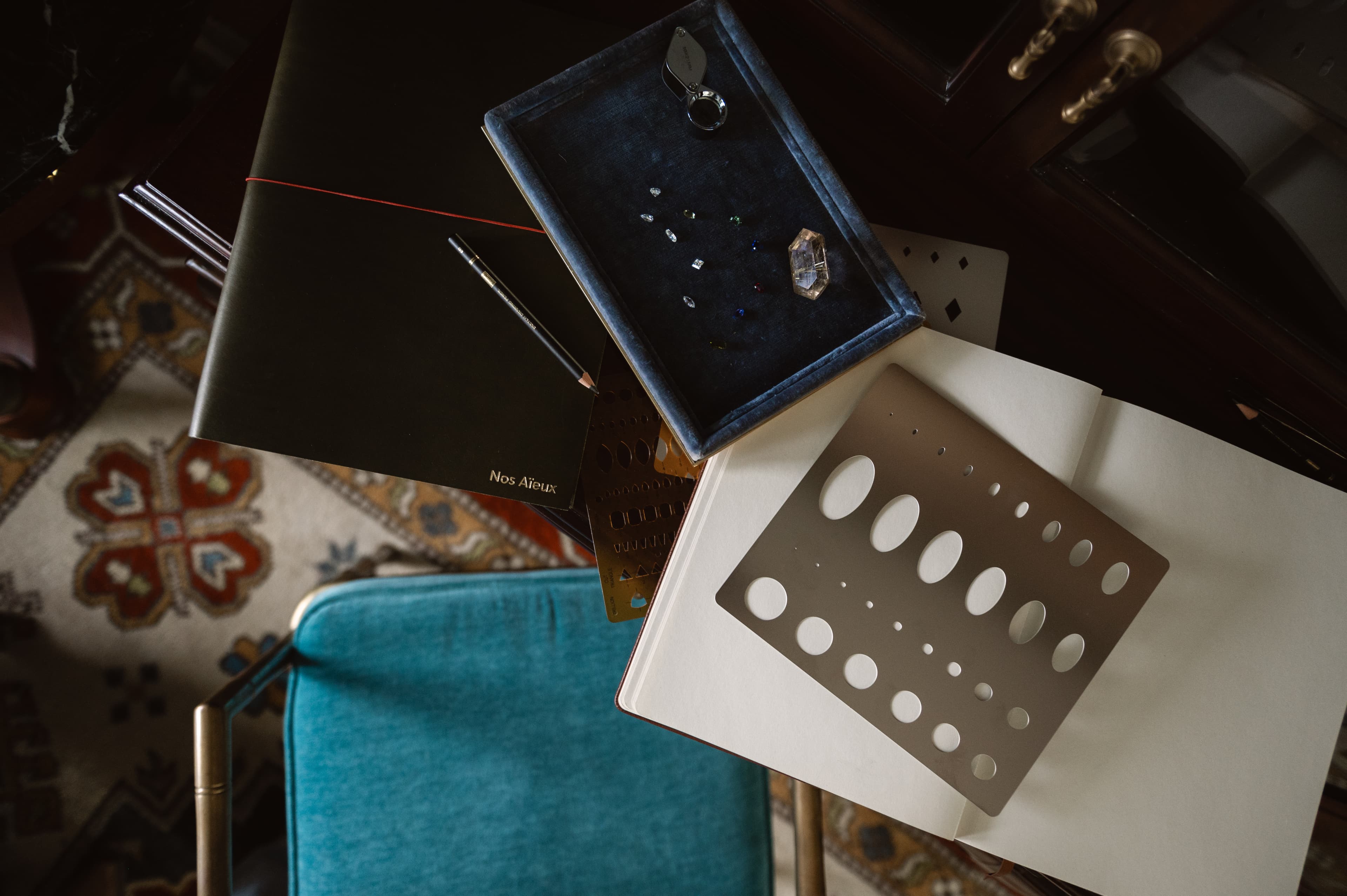 A working corner of the Nos Aïeux atelier — leather sketchbook, ring sizer, and tray of stones
