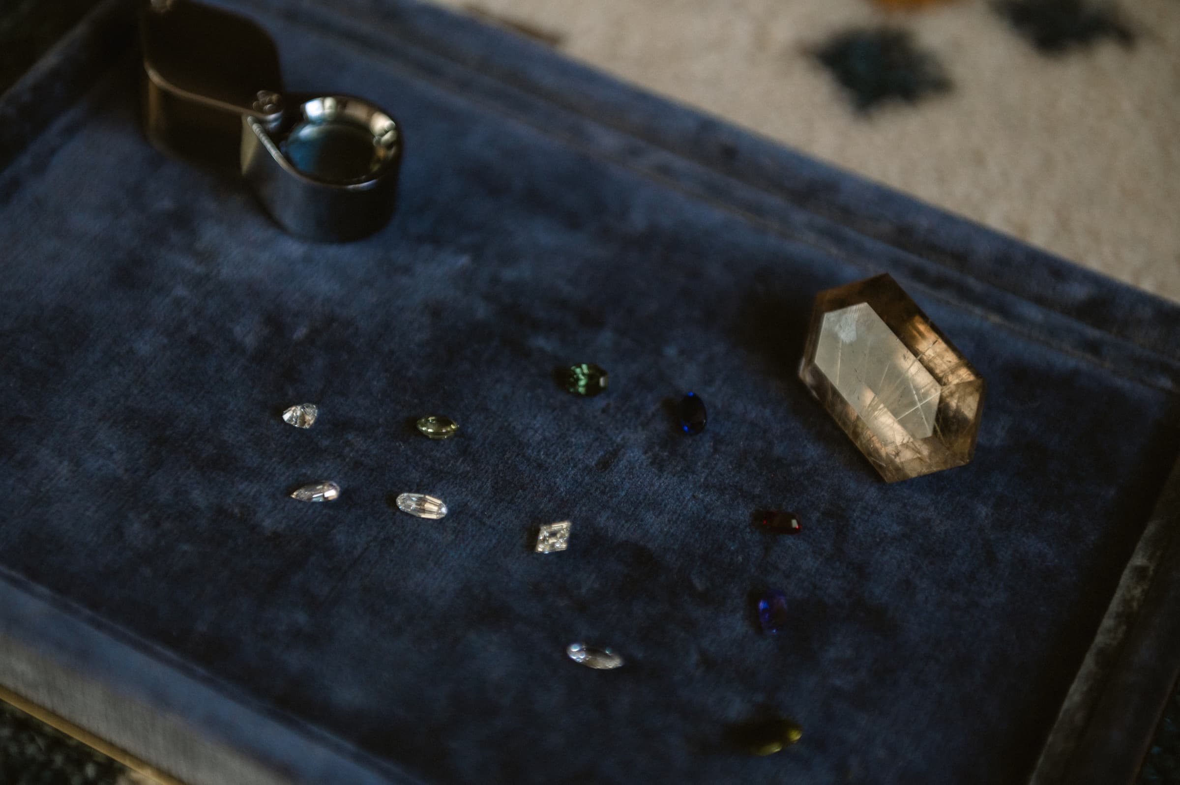Loose diamonds and coloured stones on a velvet jeweller's tray with a loupe