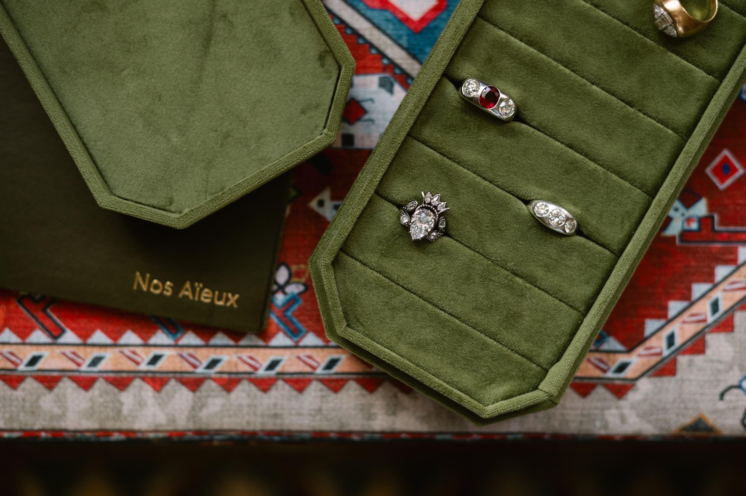 Nos Aïeux ring case — heirloom rings on olive velvet over an ancestral textile